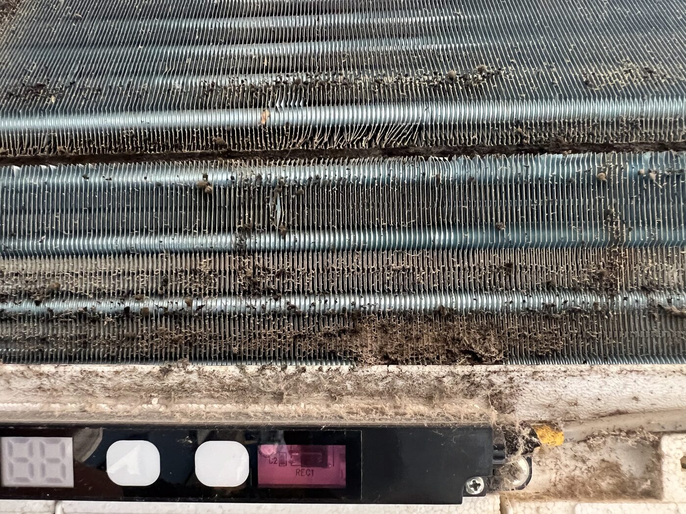Close-up of heavily contaminated AC evaporator coils with compacted dust and organic matter between the fins.